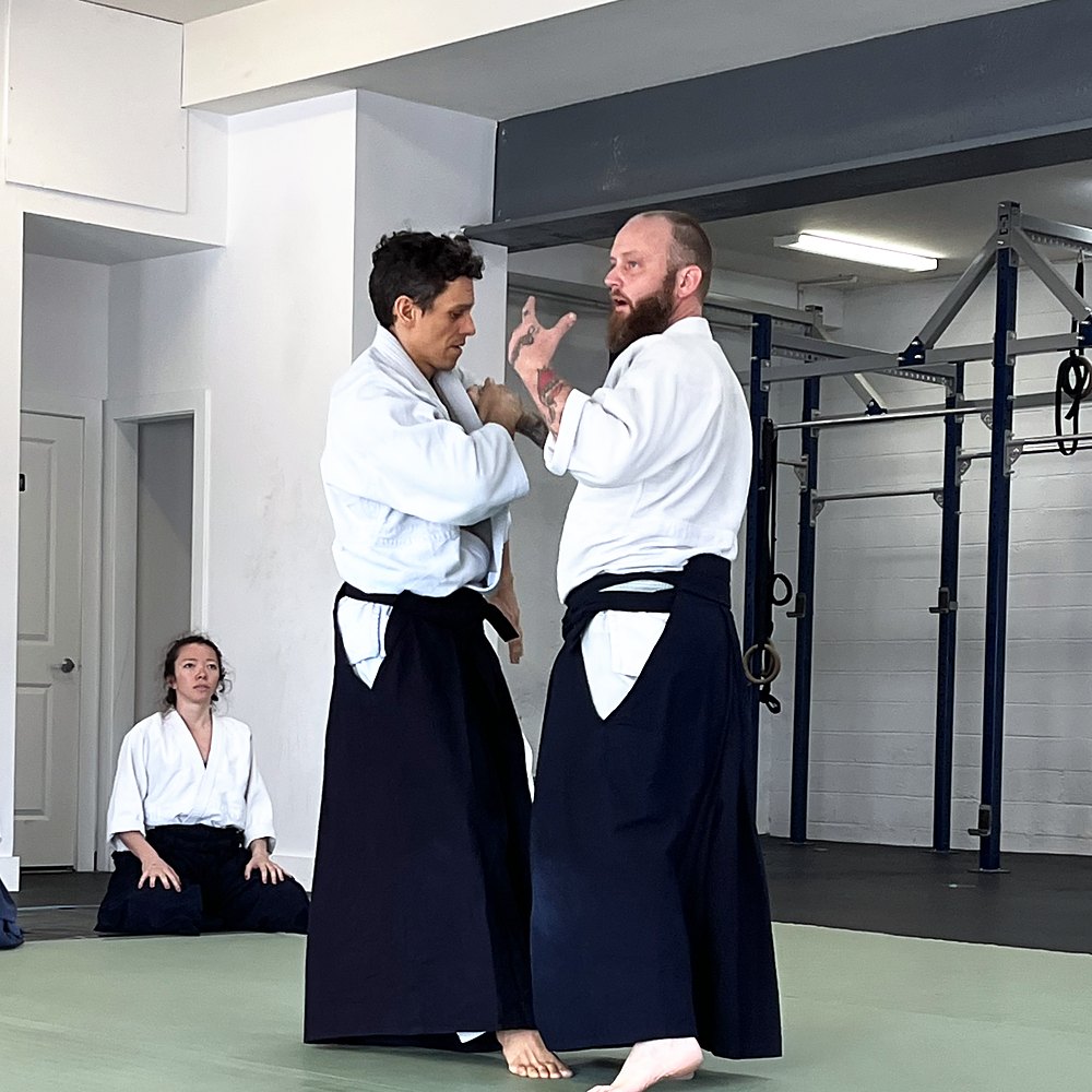 An instructor demonstrating an entry on a partner while two students kneel and watch