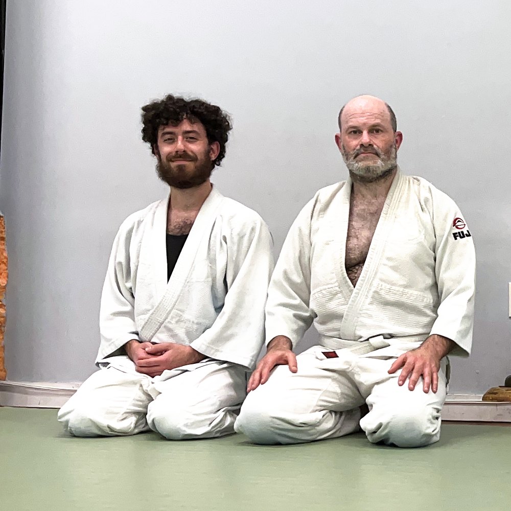 Two students a generation apart kneeling side by side after class