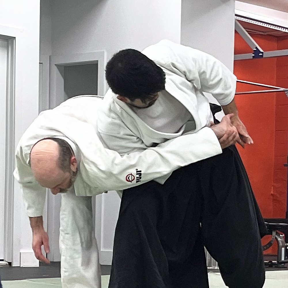 A student in hakama applying an arm lock that bends his partner forward